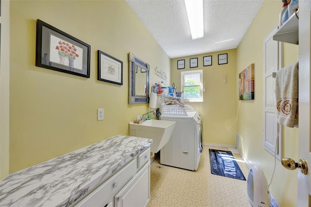 laundry area featuring washing machine and clothes dryer, light floors, cabinet space, a textured ceiling, and a sink