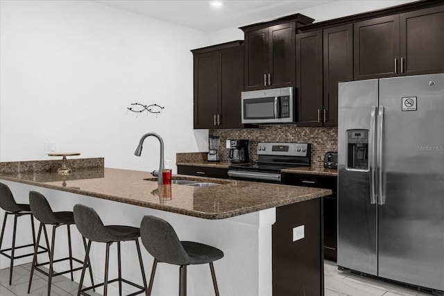 kitchen featuring a breakfast bar, backsplash, sink, dark stone counters, and stainless steel appliances