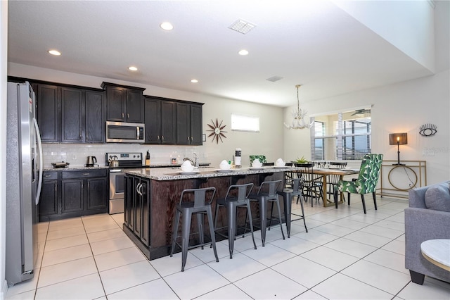 kitchen with a kitchen island with sink, a kitchen breakfast bar, light stone countertops, hanging light fixtures, and appliances with stainless steel finishes