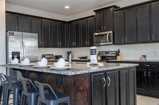 kitchen with a center island with sink, stainless steel appliances, dark brown cabinets, and light tile patterned flooring