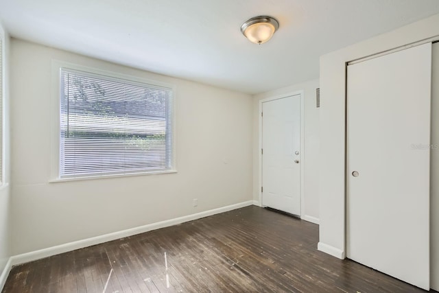 unfurnished bedroom featuring dark wood-type flooring, a closet, visible vents, and baseboards