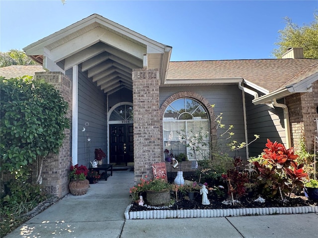 entrance to property with brick siding and a shingled roof