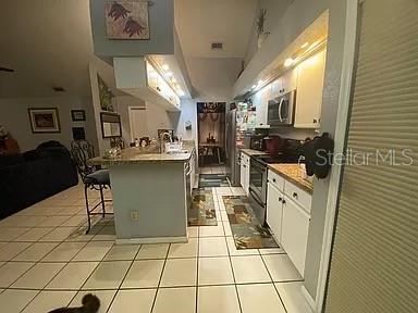 kitchen featuring a kitchen bar, open floor plan, stainless steel appliances, a peninsula, and light tile patterned flooring