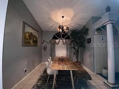 unfurnished dining area with baseboards, lofted ceiling, decorative columns, tile patterned floors, and a notable chandelier