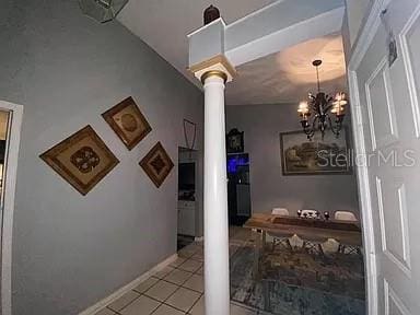 corridor featuring decorative columns, an inviting chandelier, and light tile patterned flooring