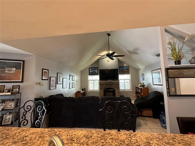 living area with tile patterned floors, ceiling fan, a fireplace, and vaulted ceiling