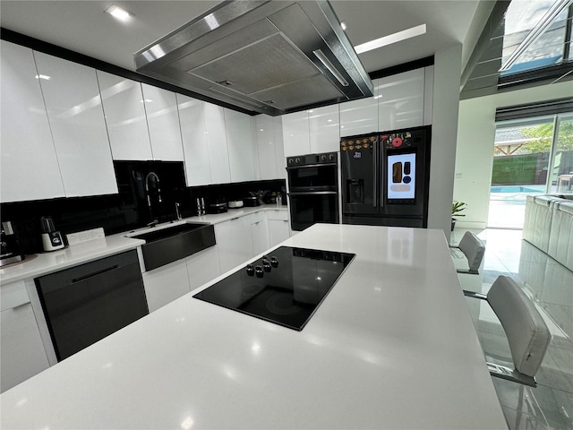 kitchen with tasteful backsplash, island range hood, white cabinetry, sink, and black appliances