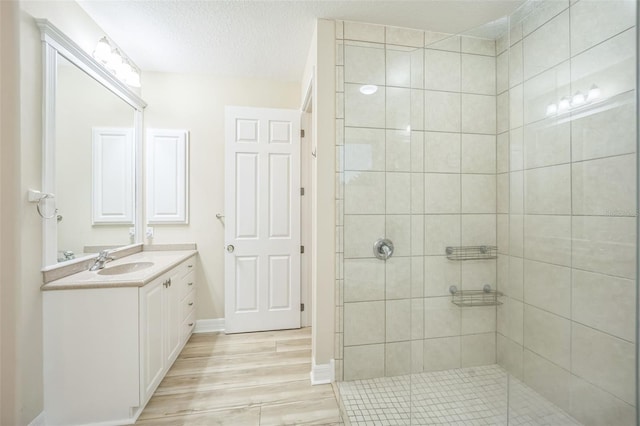 bathroom with vanity, a textured ceiling, wood-type flooring, and tiled shower