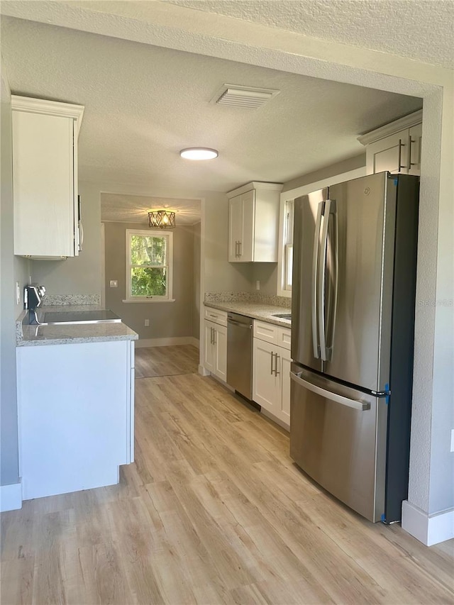 kitchen with stainless steel appliances, light wood-style floors, white cabinets, a textured ceiling, and baseboards