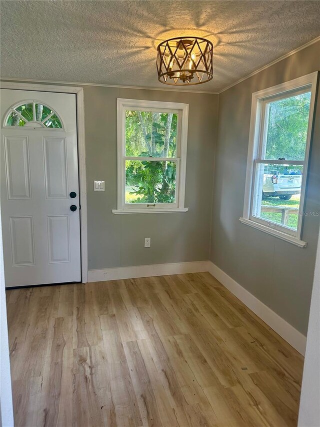 entrance foyer with ornamental molding, light wood-type flooring, a textured ceiling, and baseboards