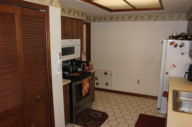 kitchen with light tile patterned floors, dark brown cabinetry, and white appliances