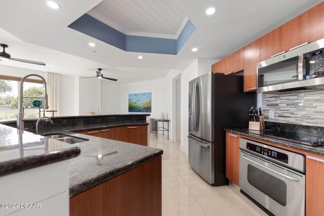 231 Riverside Dr Unit 101-1, Holly Hill, FL 32117 - kitchen featuring appliances with stainless steel finishes, a ceiling fan, a raised ceiling, decorative backsplash, and brown cabinetry