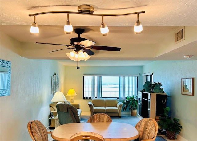 dining area featuring ceiling fan, a textured ceiling, carpet floors, and a tray ceiling