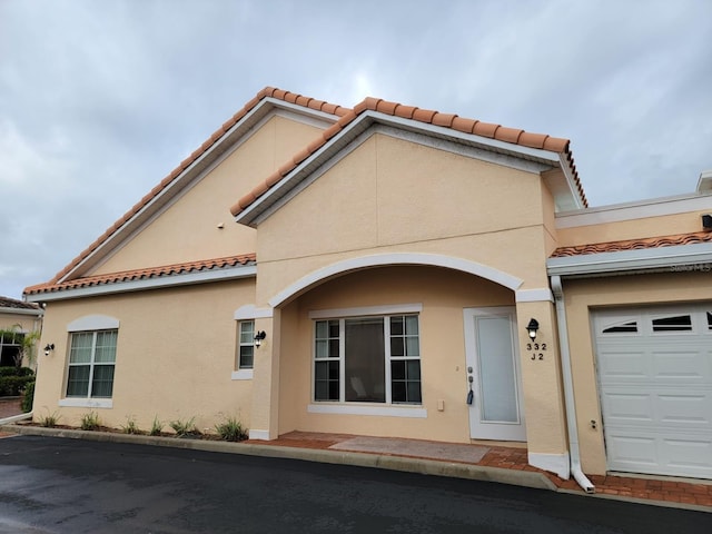 mediterranean / spanish home with a garage, a tiled roof, and stucco siding