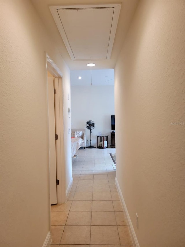 hall with light tile patterned flooring, attic access, and baseboards