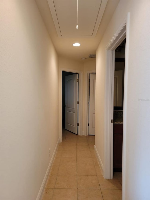 hall with light tile patterned floors, visible vents, attic access, and baseboards