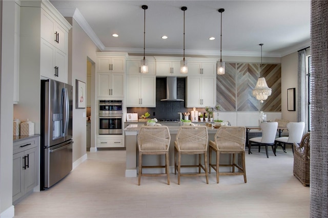 kitchen with a center island with sink, wall chimney range hood, appliances with stainless steel finishes, a kitchen bar, and hanging light fixtures