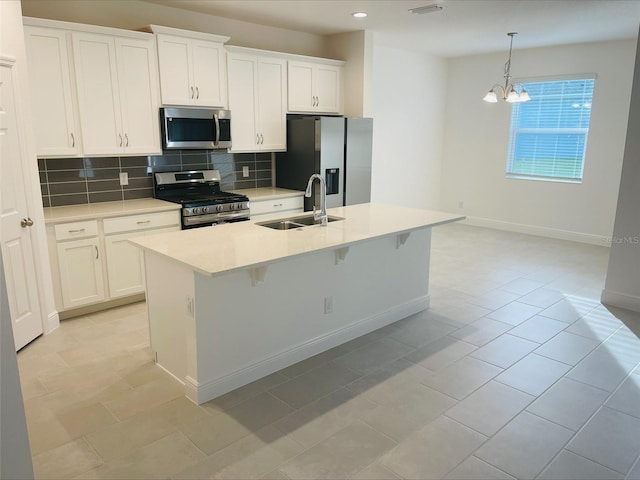 kitchen with appliances with stainless steel finishes, an island with sink, hanging light fixtures, and white cabinets