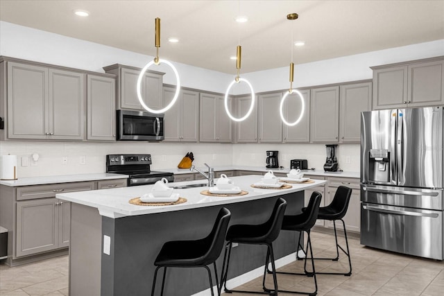 kitchen with gray cabinets, hanging light fixtures, appliances with stainless steel finishes, light tile patterned floors, and a center island with sink