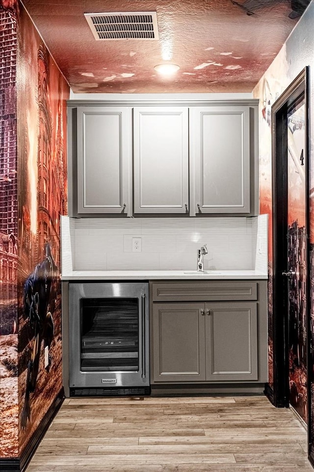 bar featuring light wood-type flooring, beverage cooler, sink, and gray cabinetry