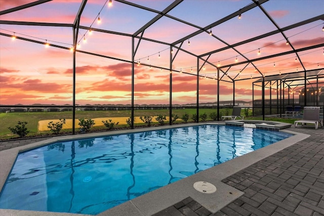 pool at dusk with a patio area, an in ground hot tub, and a lanai