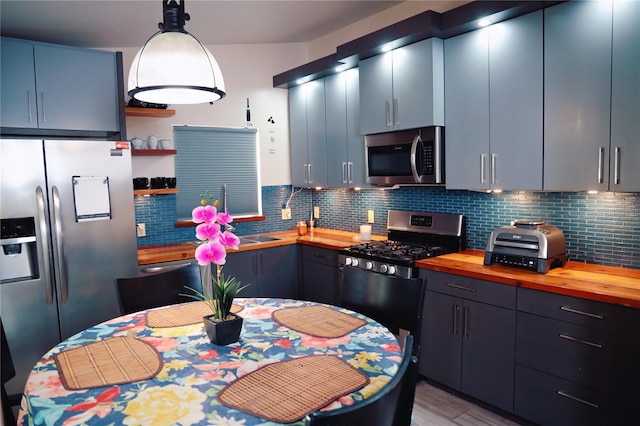 kitchen featuring butcher block countertops, blue cabinets, pendant lighting, appliances with stainless steel finishes, and tasteful backsplash