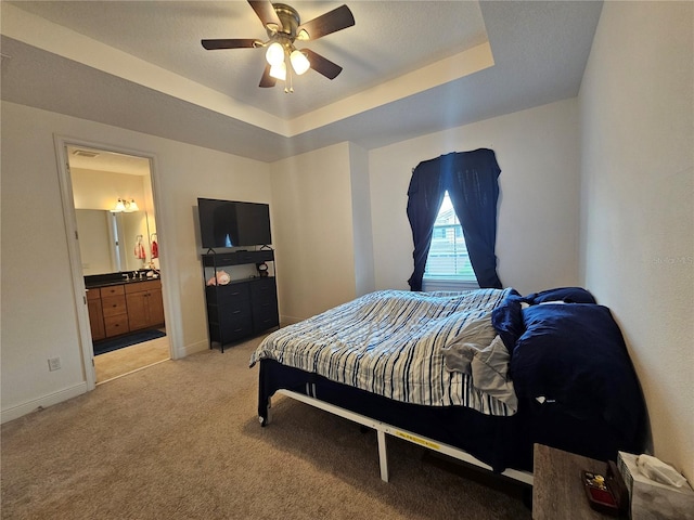 bedroom featuring a raised ceiling, light colored carpet, connected bathroom, and ceiling fan