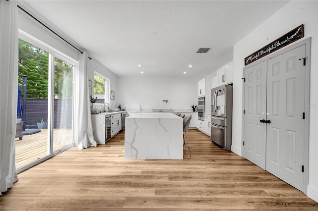 kitchen featuring white cabinets, a kitchen island, stainless steel appliances, and light hardwood / wood-style flooring