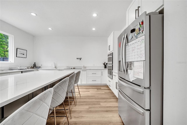 kitchen with appliances with stainless steel finishes, a breakfast bar, light stone counters, light wood-type flooring, and white cabinets