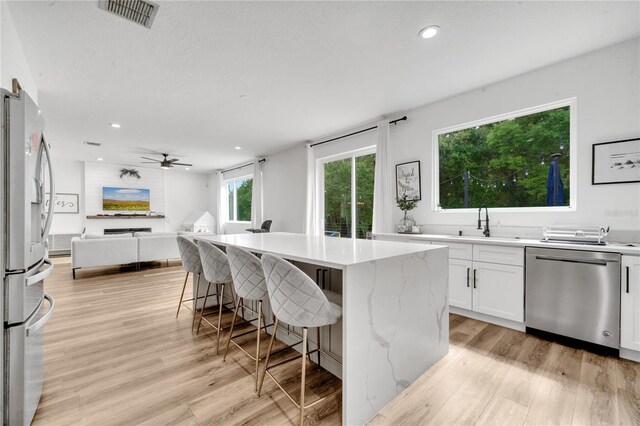 kitchen with light hardwood / wood-style flooring, appliances with stainless steel finishes, a breakfast bar, a center island, and white cabinetry