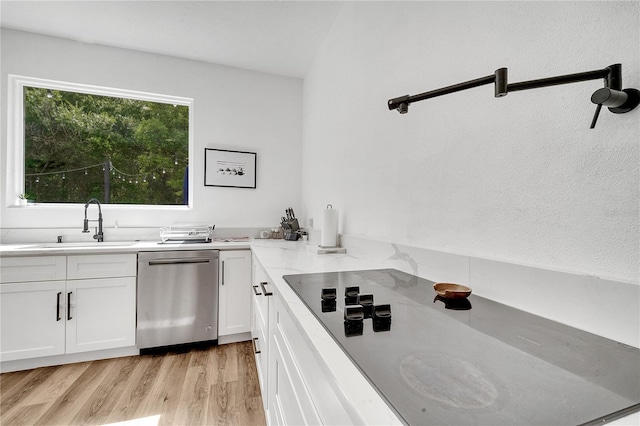 kitchen featuring light wood-type flooring, black electric stovetop, white cabinetry, dishwasher, and sink