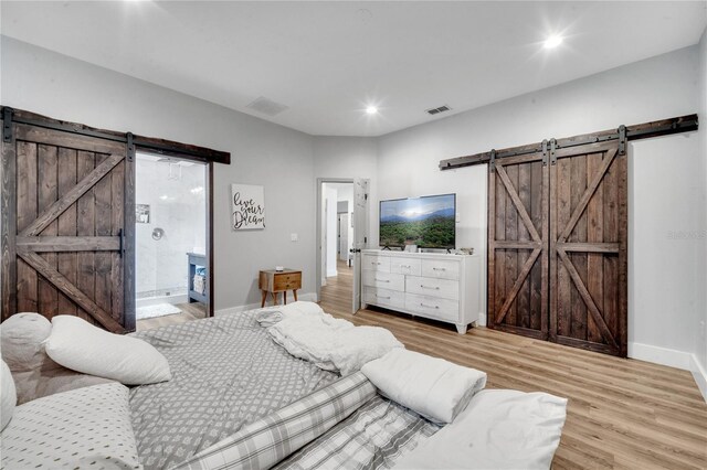 bedroom with a barn door, ensuite bathroom, and light hardwood / wood-style floors