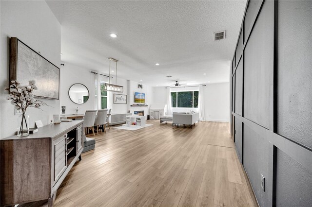 living room with a textured ceiling, light hardwood / wood-style flooring, and ceiling fan