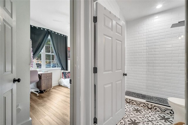 bathroom with tiled shower, toilet, and hardwood / wood-style flooring