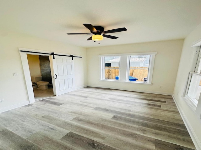 unfurnished bedroom with a barn door, light hardwood / wood-style floors, ceiling fan, and connected bathroom