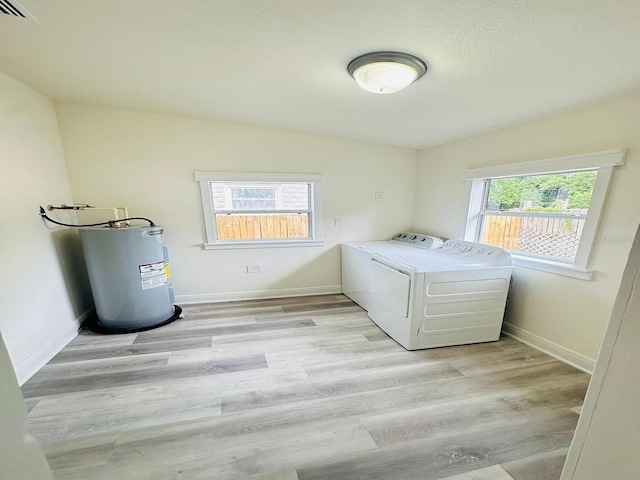 clothes washing area with a textured ceiling, electric water heater, independent washer and dryer, and light hardwood / wood-style floors