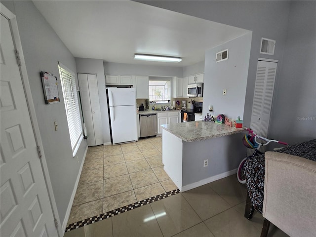 kitchen with kitchen peninsula, light tile patterned floors, appliances with stainless steel finishes, and white cabinets