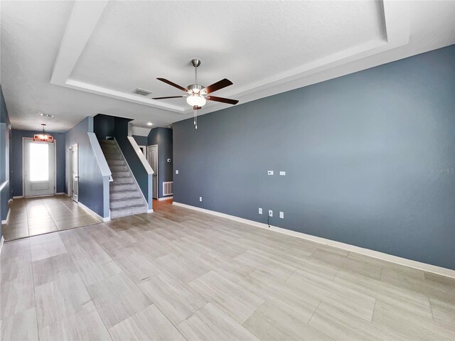 tiled empty room with ceiling fan and a tray ceiling