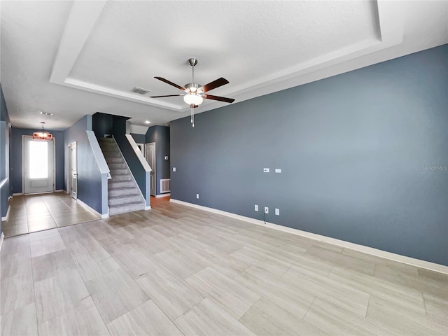 unfurnished living room featuring stairway, visible vents, a tray ceiling, and baseboards