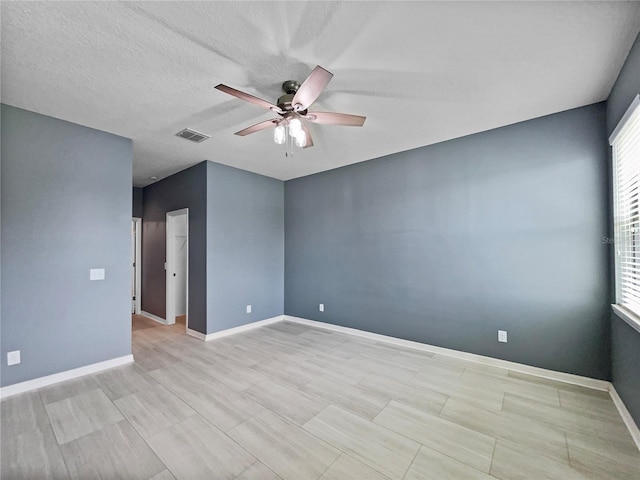 unfurnished room with a ceiling fan, visible vents, a textured ceiling, and baseboards