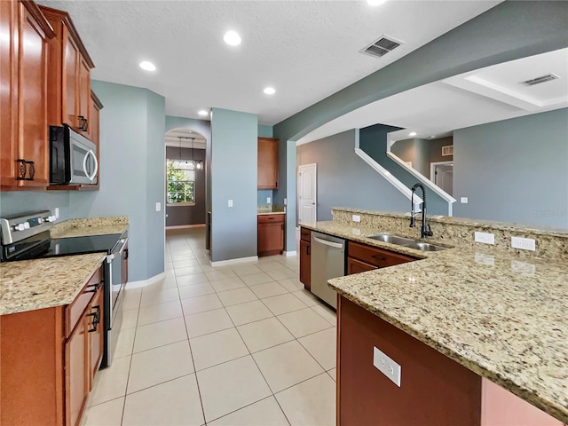 kitchen featuring light stone counters, arched walkways, visible vents, appliances with stainless steel finishes, and a sink