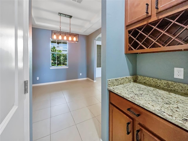 kitchen featuring arched walkways, light stone counters, hanging light fixtures, brown cabinets, and a tray ceiling