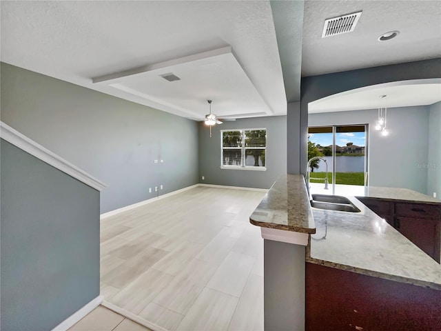 kitchen featuring ceiling fan, a sink, visible vents, baseboards, and decorative light fixtures