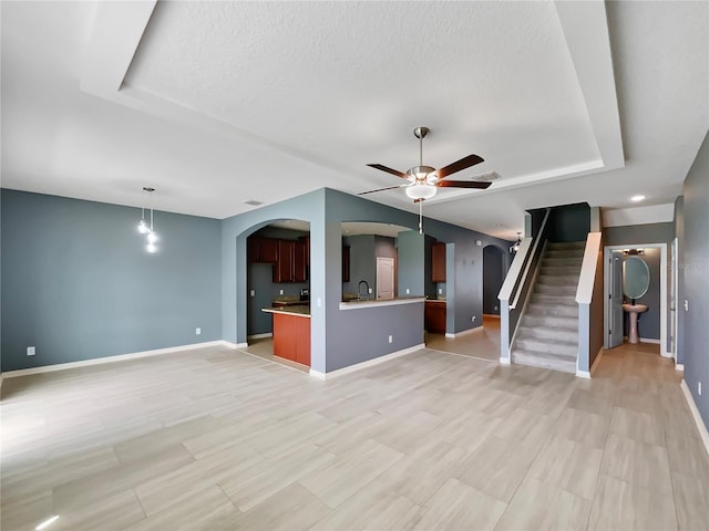 unfurnished living room with a ceiling fan, stairway, arched walkways, and a sink