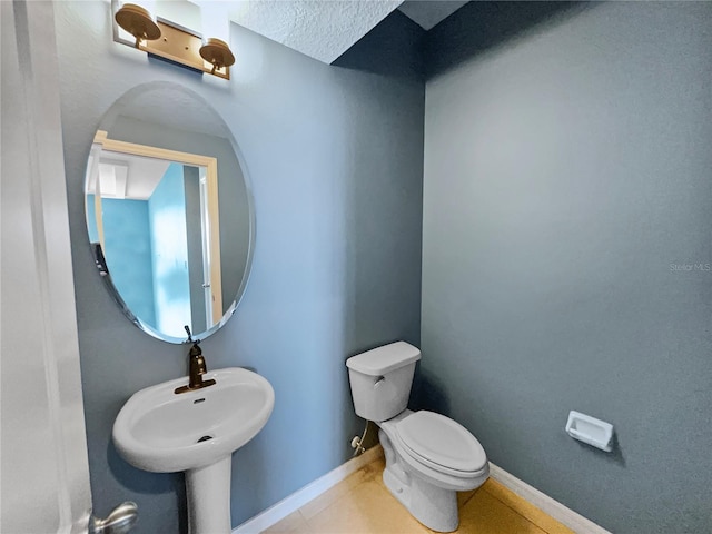 half bath featuring toilet, tile patterned flooring, baseboards, and a sink