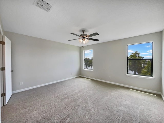 carpeted spare room featuring a ceiling fan, visible vents, and baseboards