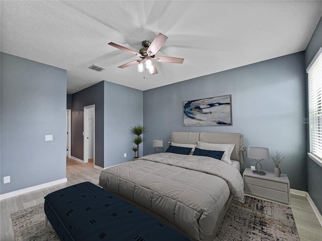 bedroom with ceiling fan, a textured ceiling, visible vents, baseboards, and light wood finished floors