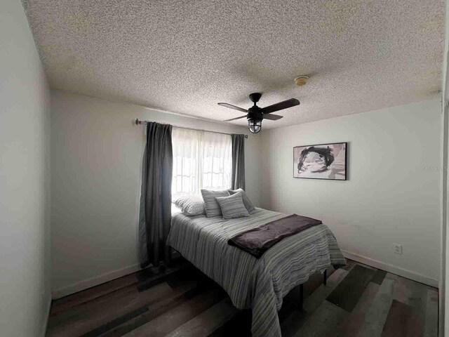 bedroom with dark wood-type flooring, a textured ceiling, and ceiling fan