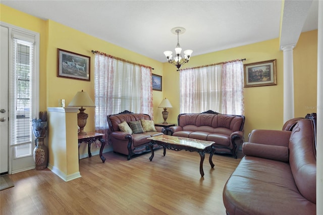 living room featuring decorative columns, an inviting chandelier, and light hardwood / wood-style floors