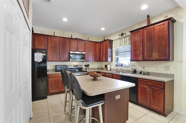 kitchen with black appliances, a kitchen breakfast bar, a kitchen island, and light tile patterned flooring